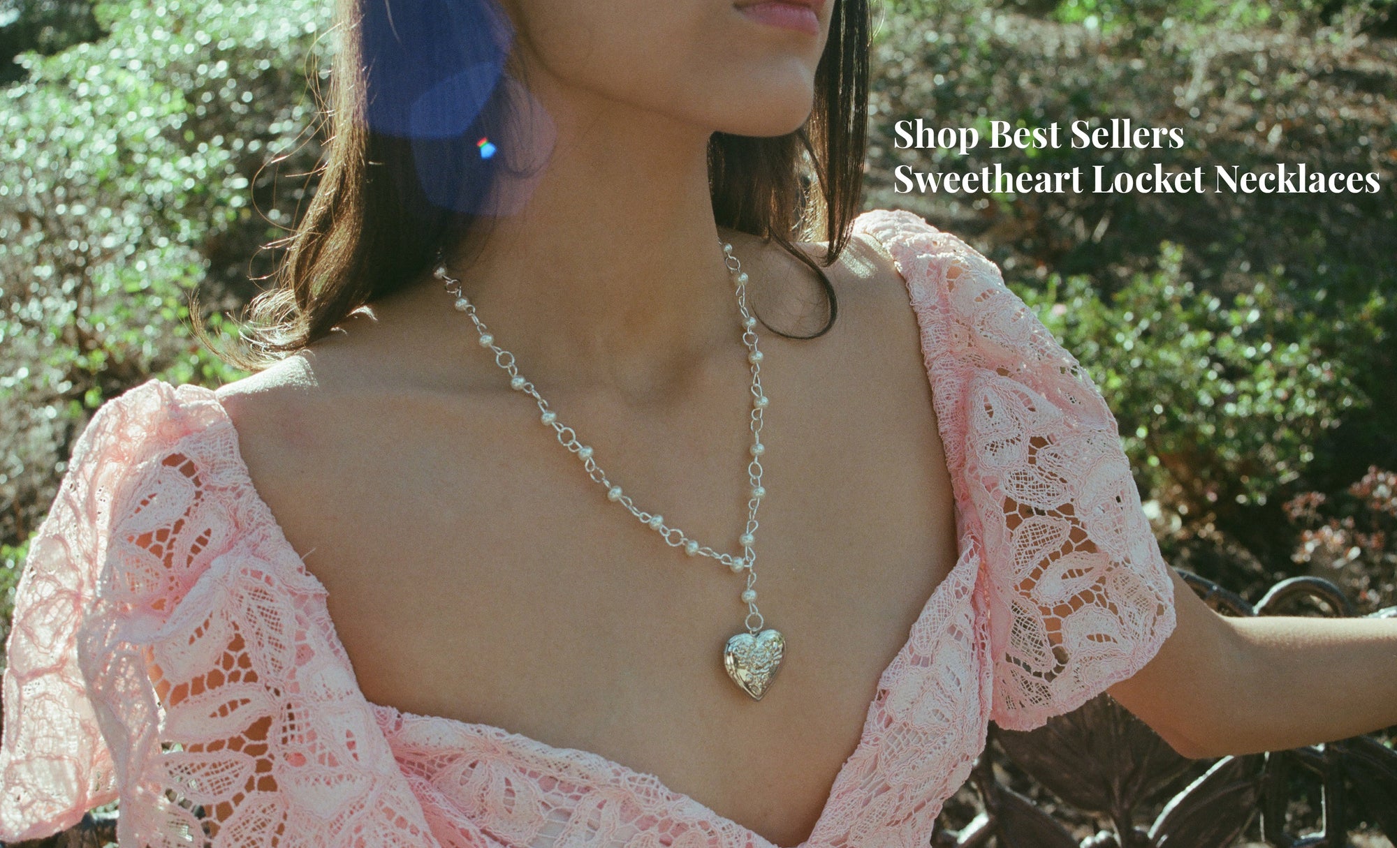 Woman wearing a pink lace top and heart-shaped necklace outdoors
